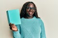 African young woman reading a book wearing glasses looking positive and happy standing and smiling with a confident smile showing Royalty Free Stock Photo