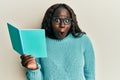 African young woman reading a book wearing glasses scared and amazed with open mouth for surprise, disbelief face Royalty Free Stock Photo