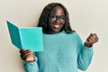African young woman reading a book wearing glasses screaming proud, celebrating victory and success very excited with raised arm Royalty Free Stock Photo