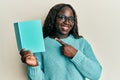 African young woman reading a book wearing glasses smiling happy pointing with hand and finger Royalty Free Stock Photo