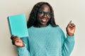 African young woman reading a book wearing glasses smiling happy pointing with hand and finger to the side Royalty Free Stock Photo