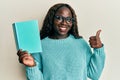 African young woman reading a book wearing glasses smiling happy and positive, thumb up doing excellent and approval sign Royalty Free Stock Photo