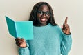 African young woman reading a book wearing glasses smiling with an idea or question pointing finger with happy face, number one Royalty Free Stock Photo