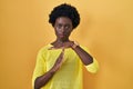 African young woman standing over yellow studio doing time out gesture with hands, frustrated and serious face Royalty Free Stock Photo