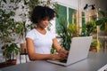 African young woman working typing on laptop computer sitting at desk in home office room with modern biophilia design Royalty Free Stock Photo