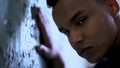 Afro-american boy leaning on flaky wall, poverty and life difficulties, sadness