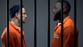 Afro-american and caucasian inmates looking at each other in cell, conflict