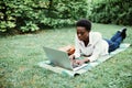 Afro american college student lying down on the grass working on laptop at campus. University. Royalty Free Stock Photo