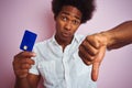 Afro american customer man holding credit card standing over isolated pink background with angry face, negative sign showing Royalty Free Stock Photo