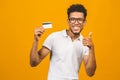 Afro american customer man holding credit card standing over isolated yellow background happy with big smile doing ok sign, thumb Royalty Free Stock Photo