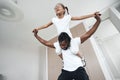 Afro American girl sits on her father's neck with her arms wide apart