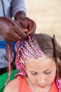 Afro American hairdresser made thin pink plaits in African style for young Caucasian girl