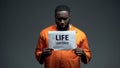 Afro-american imprisoned male holding life sentence sign, looking to camera Royalty Free Stock Photo