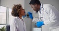 Afro-american male doctor examining young woman throat in office.