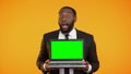 Afro-american male in formal suit holding prekeyed laptop and smiling, wow