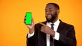 Afro-american male in suit pointing at prekeyed phone and winking, advertisement