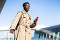 Afro-American millennial traveler man with yellow suitcase stands in airport terminal, holding phone, calling and looking for a Royalty Free Stock Photo