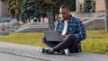 Afro american student guy african business man sitting outdoors in city street typing on laptop working online with Royalty Free Stock Photo