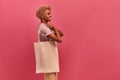 Afro american woman standing on pink background with eco bag on her shoulders.