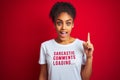 Afro american woman wearing funny t-shirt with irony comments over isolated red background surprised with an idea or question