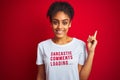 Afro american woman wearing funny t-shirt with irony comments over isolated red background very happy pointing with hand and