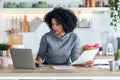 Afro business woman working with computer while consulting some invoices and documents in the kitchen at home Royalty Free Stock Photo