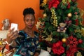 Afro-descendant Colombian woman sitting on the sofa next to the Christmas tree with her cell phone