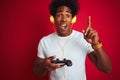 Afro gamer man playing video game using joystick headphones over isolated red background surprised with an idea or question Royalty Free Stock Photo