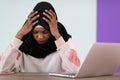 afro girl wearing a hijab is disappointed and sad sitting in her home office and using a laptop Royalty Free Stock Photo