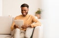 Afro Guy Using Tablet Computer Sitting On Couch At Home Royalty Free Stock Photo