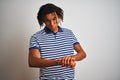 Afro man with dreadlocks wearing striped blue polo standing over isolated white background Checking the time on wrist watch, Royalty Free Stock Photo