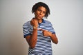 Afro man with dreadlocks wearing striped blue polo standing over isolated white background In hurry pointing to watch time, Royalty Free Stock Photo