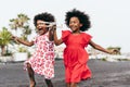 Afro twins sisters running on the beach while playing with wood toy airplane - Youth lifestyle and travel concept - Main focus on
