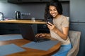 Afro beautiful woman using laptop and mobile phone while having breakfast in modern kitchen Royalty Free Stock Photo