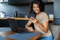 Afro beautiful woman using laptop and mobile phone while having breakfast in modern kitchen Royalty Free Stock Photo