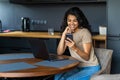 Afro beautiful woman using laptop and mobile phone while having breakfast in modern kitchen Royalty Free Stock Photo