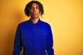 Afro worker man with dreadlocks wearing mechanic uniform over isolated yellow background making fish face with lips, crazy and Royalty Free Stock Photo