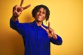 Afro worker man with dreadlocks wearing mechanic uniform over isolated yellow background smiling looking to the camera showing Royalty Free Stock Photo