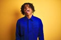 Afro worker man with dreadlocks wearing mechanic uniform over isolated yellow background sticking tongue out happy with funny Royalty Free Stock Photo