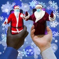 Afroamerican and caucasian-white hands holding phones with 2 Santa Clauses. Royalty Free Stock Photo