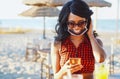 Afroamerican girl using smartphone in beach - Girl sitting in a bar with lower face mask on similing and drinking