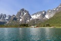 Against a backdrop of Lofoten\'s jagged peaks, a remote farm with vibrant red roofs stands out along the shimmering shoreline Royalty Free Stock Photo