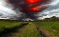 Dramatic stormy sky over a green field and dirt road Royalty Free Stock Photo