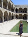 A woman stands against the background of an ancient building with her back turned