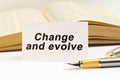 Against the background of the book lies a pen and a business card with the inscription - Change and evolve
