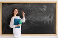 Against the background of a clean chalk board, a Caucasian lady stands and holds a notebook in her hands. the index Royalty Free Stock Photo