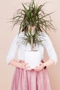 Against the background of milky coffee color, the girl is holding a potted plant in her hands. Girl`s face is covered by a plant Royalty Free Stock Photo