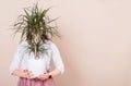 Against the background of milky coffee color, the girl is holding a potted plant in her hands. Girl`s face is covered by a plant Royalty Free Stock Photo