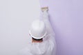 Against the background of a painted wall, the hand of a worker in a white protective helmet, holding a brush, rear view Royalty Free Stock Photo