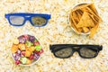 Against the background of popcorn grains two cups with different flavors of corn and glasses for the cinema Royalty Free Stock Photo